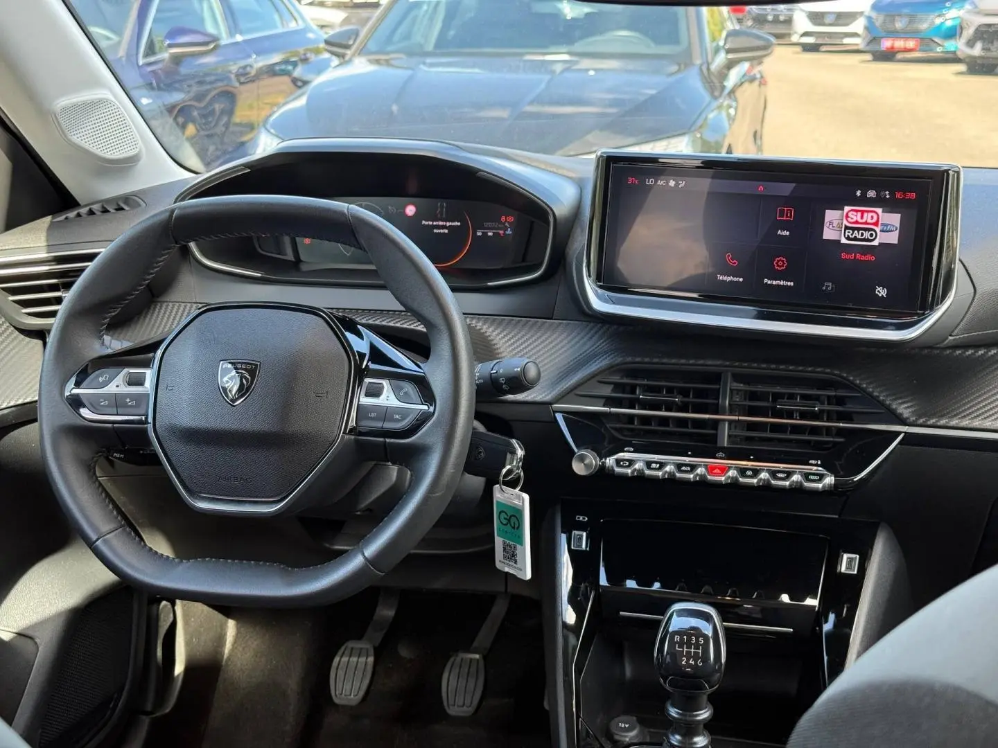 Vue intérieure avant centrée sur le volant compact et l'écran tactile du tableau de bord d'une Peugeot 208 gris Artense.