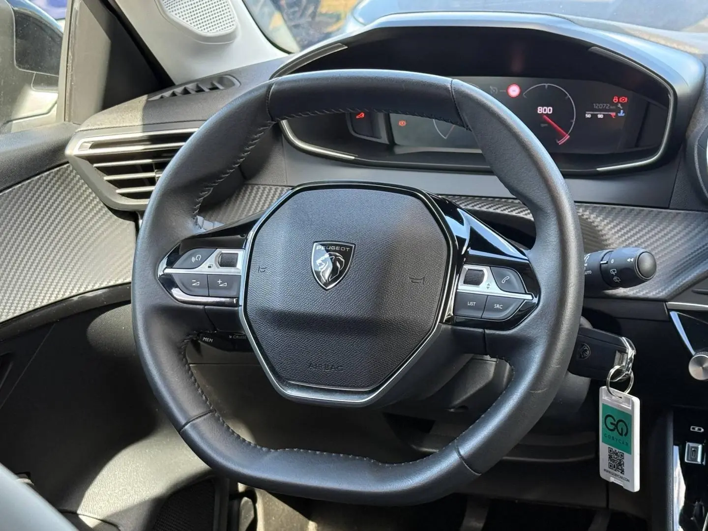 Vue rapprochée du volant noir du Peugeot 208 2025 avec tableau de bord numérique et commandes intégrées.