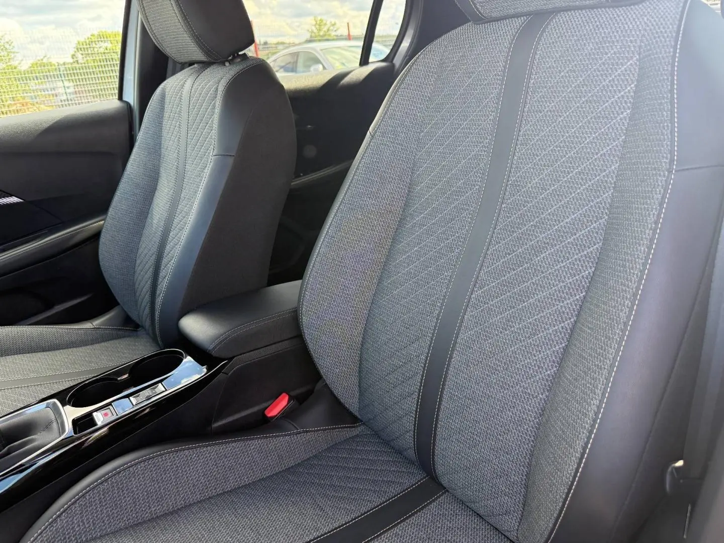 Vue rapprochée des sièges avant en tissu gris avec surpiqûres, accoudoir central et console noire brillante Peugeot 208 2025.