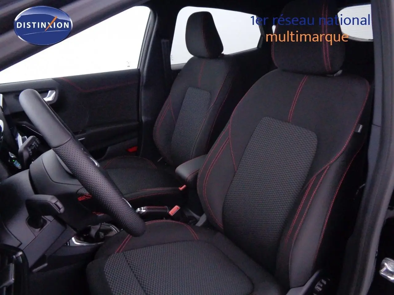 Intérieur avant du Ford Puma noir agate 2022 montrant sièges tissu noir avec surpiqûres rouges et volant cuir perforé.