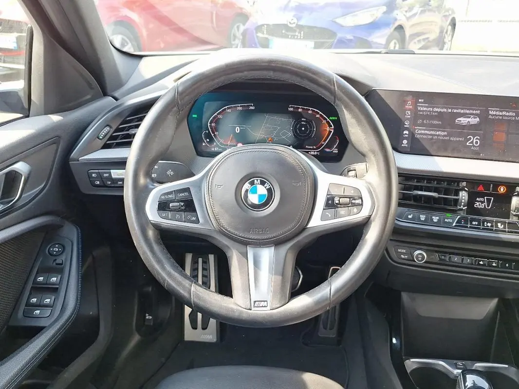 Vue intérieure centrée sur le volant cuir multifonctions et tableau de bord numérique d'une BMW Série 1 blanche 2021.