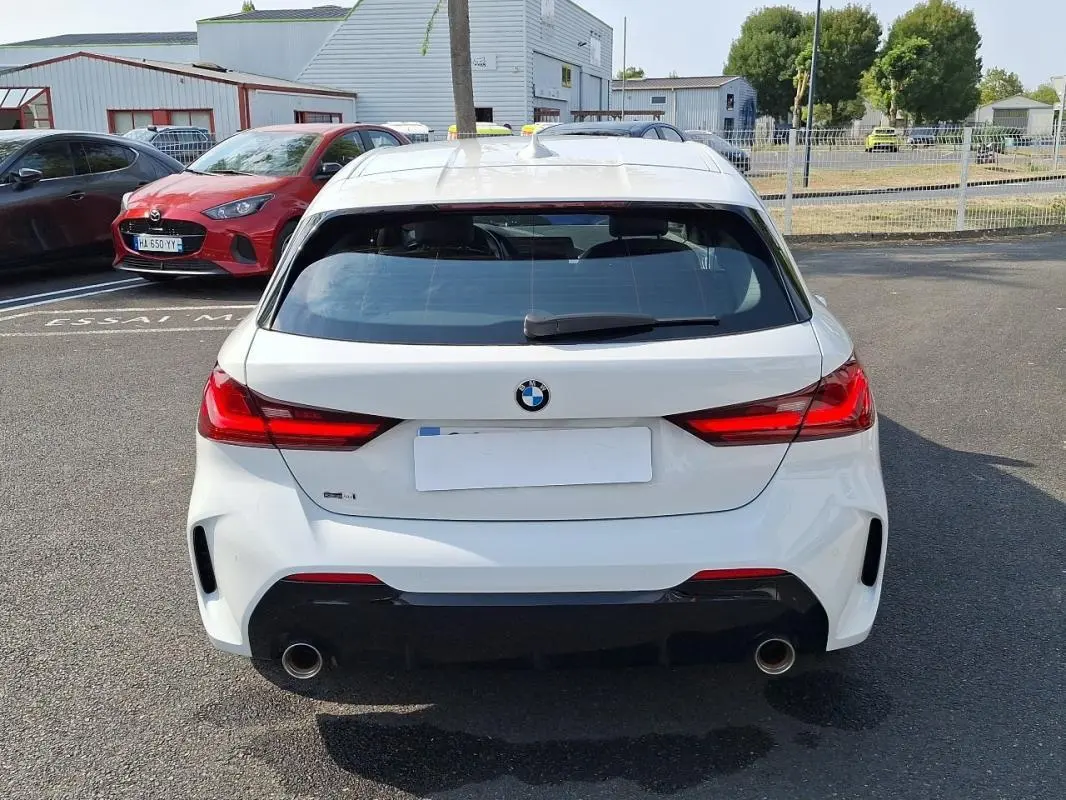 Vue arrière d'une BMW Série 1 blanche 120i M Sport 2021 avec feux rouges allumés et double sortie d'échappement chromée.
