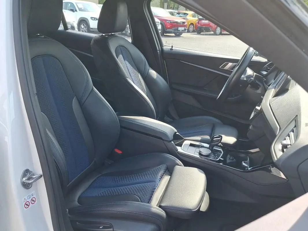 Vue intérieure côté conducteur d'une BMW Série 1 blanche 120i M Sport 2021 avec sièges sport cuir et alcantara.