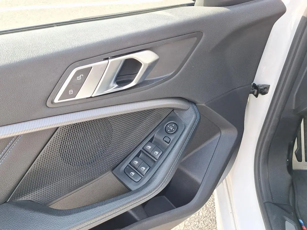 Gros plan sur la porte avant gauche blanche d'une BMW Série 1 120i M Sport, avec commandes électriques et poignée argentée.