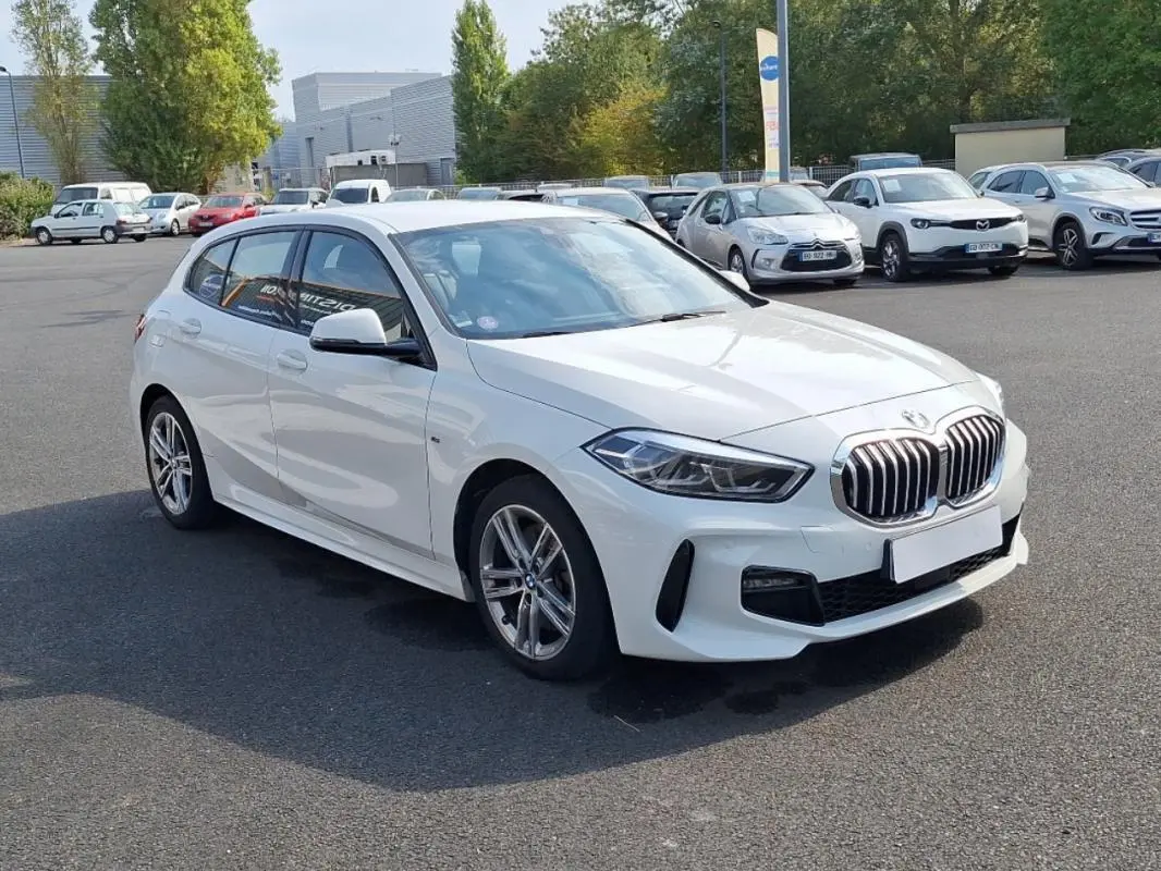 BMW Série 1 blanche vue en 3/4 avant droit, avec jantes alliage et calandre caractéristique M Sport.