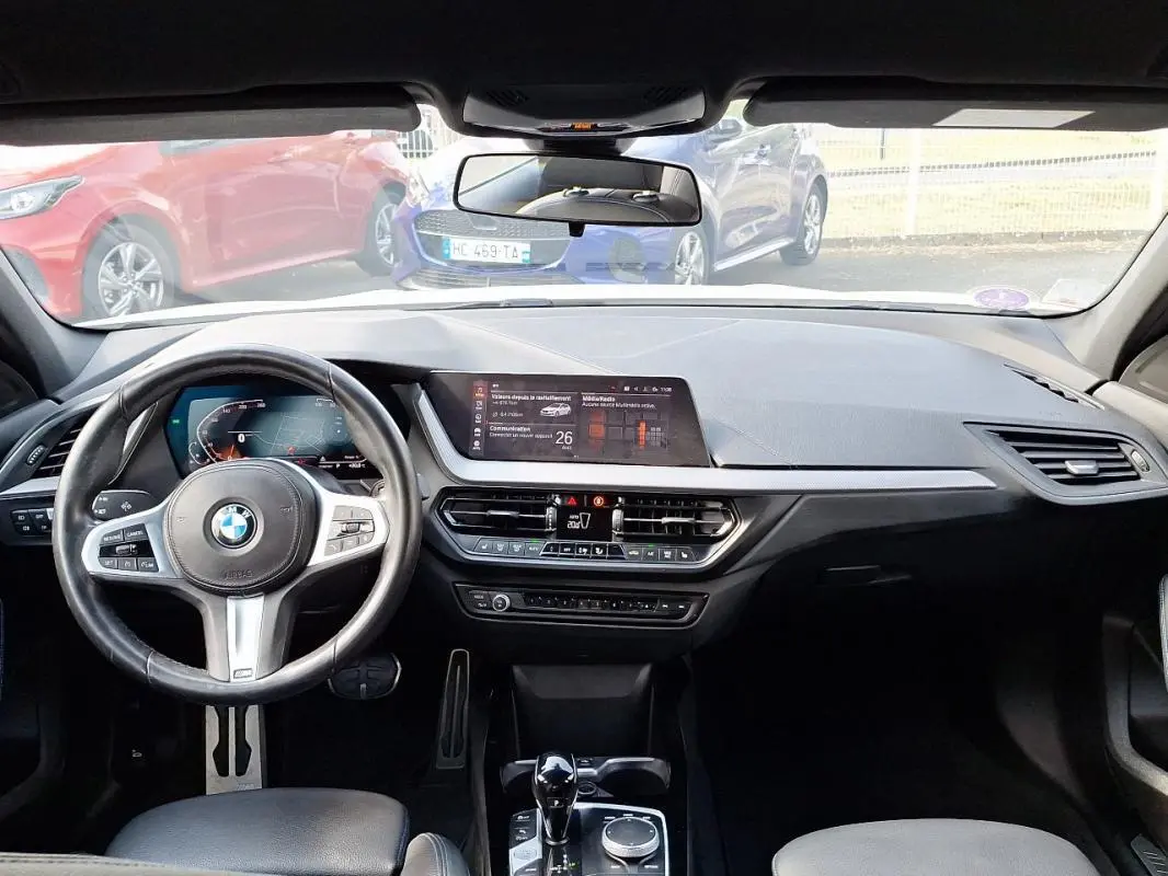 Vue intérieure de la BMW Série 1 120i M Sport 2021, tableau de bord et volant cuir multifonctions noirs.
