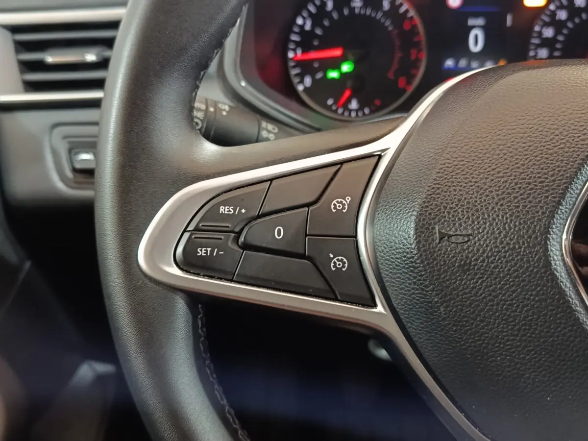 Gros plan sur le volant cuir noir de la Renault Clio 2023, avec commandes de régulateur de vitesse au côté gauche.