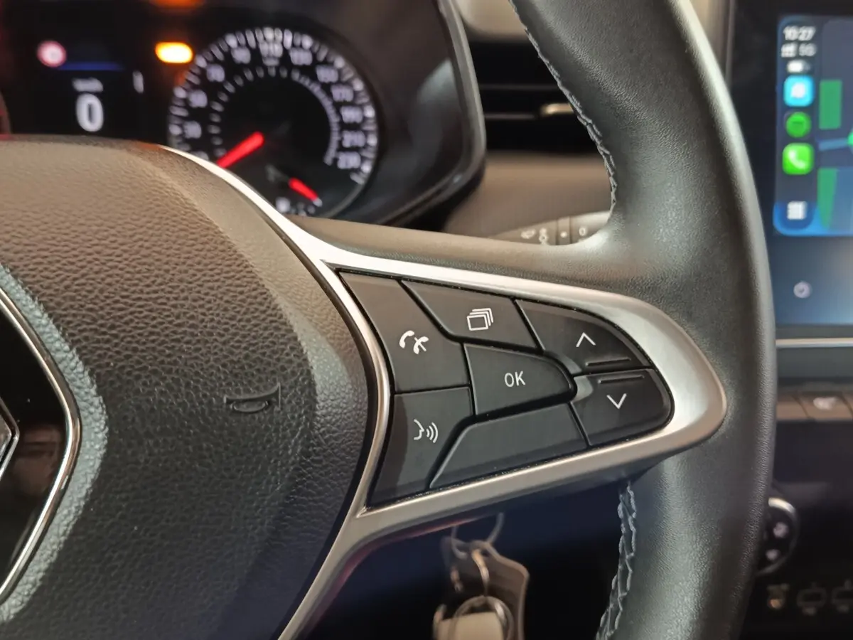 Gros plan sur les commandes multifonctions à droite du volant cuir noir de la Renault Clio gris clair 2023, avec tableau de bord partiellement visible.