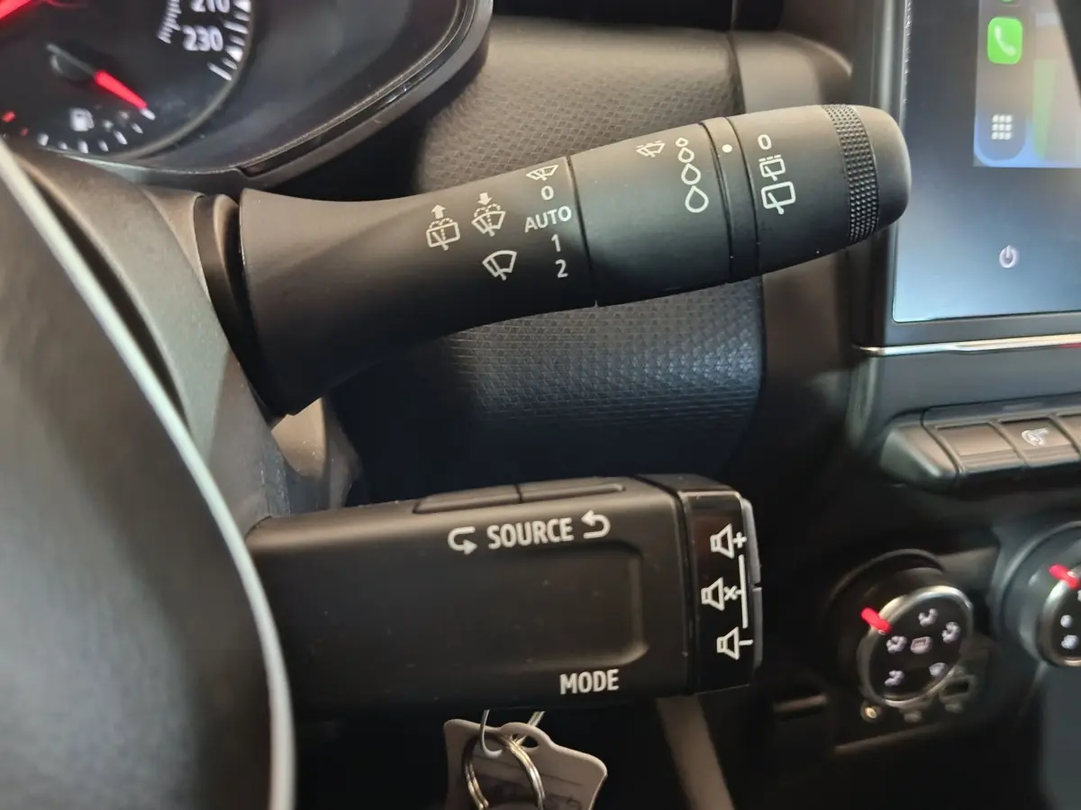 Gros plan sur les commandes au volant de la Renault Clio gris clair 2023, avec levier d'essuie-glace et multimédia.