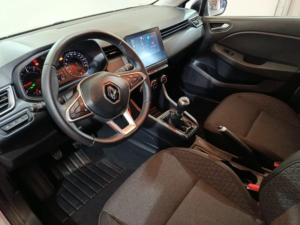 Vue intérieure côté conducteur de la Renault Clio gris clair 2023, volant cuir, écran tactile et boîte manuelle visible.