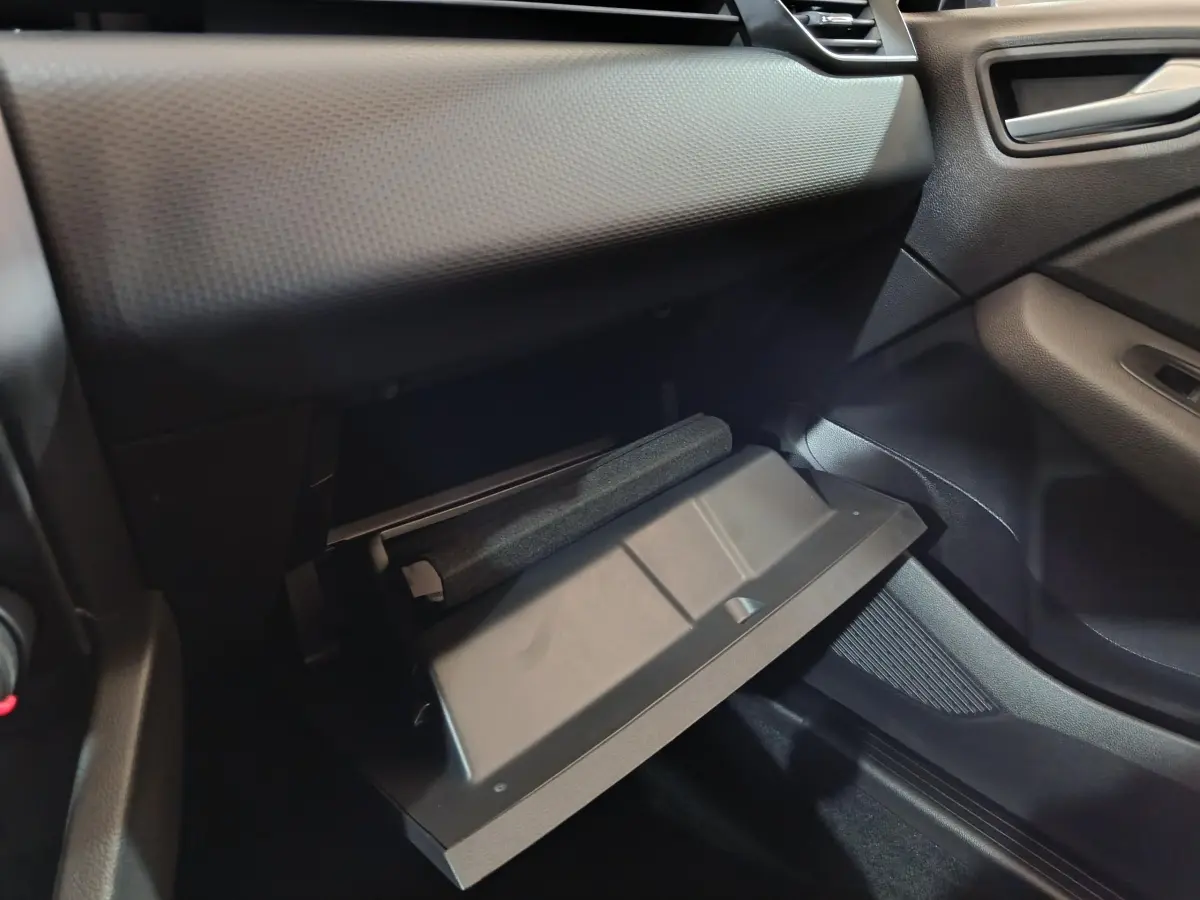 Vue intérieure côté passager de la Renault Clio gris clair 2023 avec boîte à gants ouverte et tableau de bord texturé.