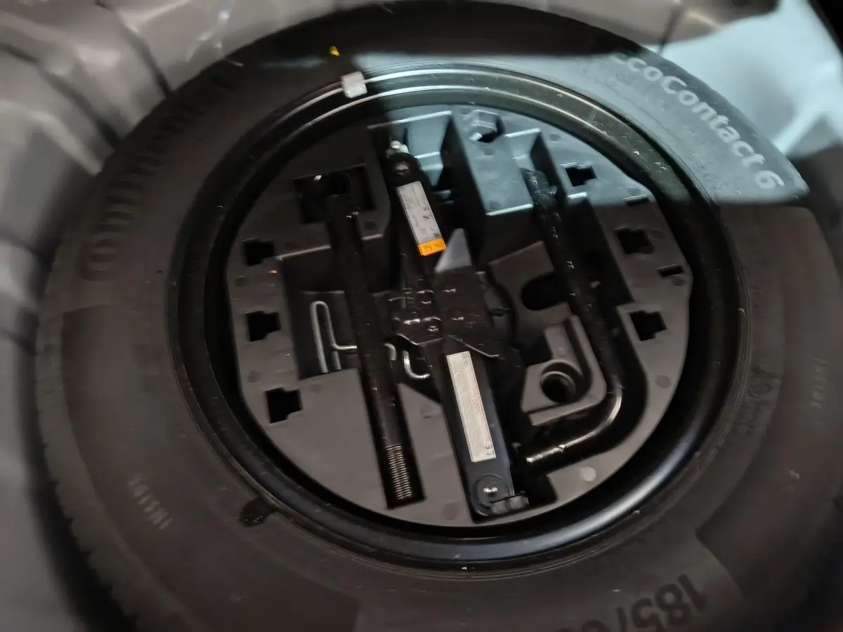 Gros plan sur la roue de secours et ses outils de bord dans le coffre de la Renault Clio gris clair 2023.