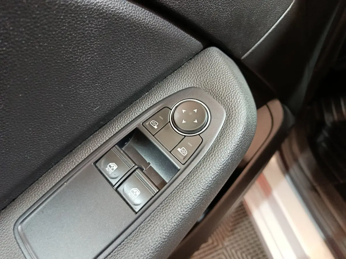 Gros plan sur les commandes de lève-vitres et rétroviseurs côté conducteur d’une Renault Clio gris clair 2023.