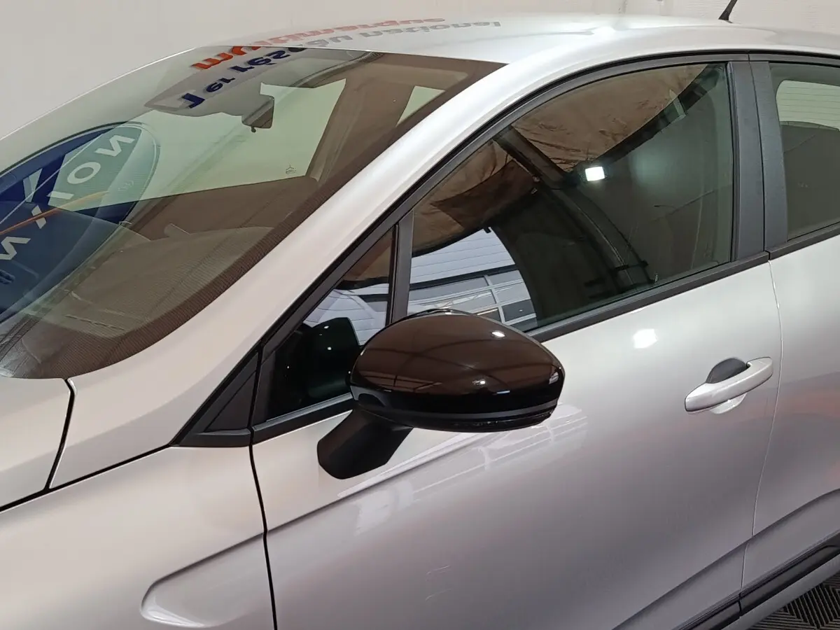 Vue côté gauche rapprochée d’une Renault Clio gris clair 2023 avec rétroviseur noir brillant et poignée de porte visible.