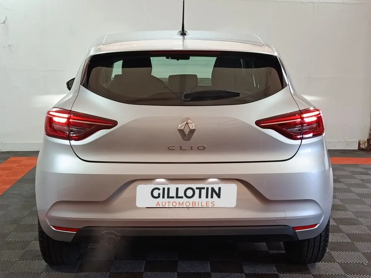 Vue arrière d'une Renault Clio gris clair 2023 avec feux LED allumés et logo central bien visible.