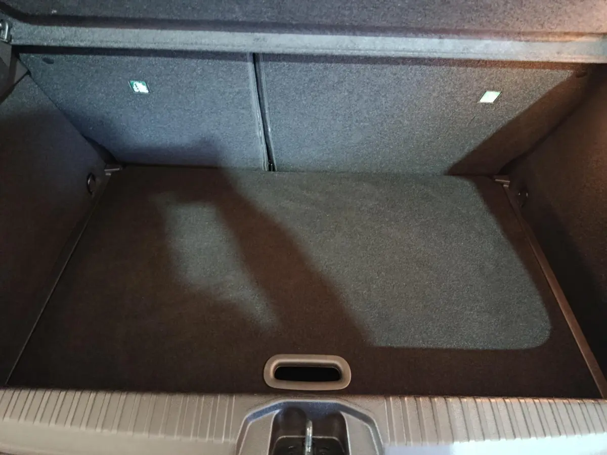 Vue plongeante sur le coffre spacieux et vide de la Renault Clio gris clair, montrant le revêtement intérieur noir.