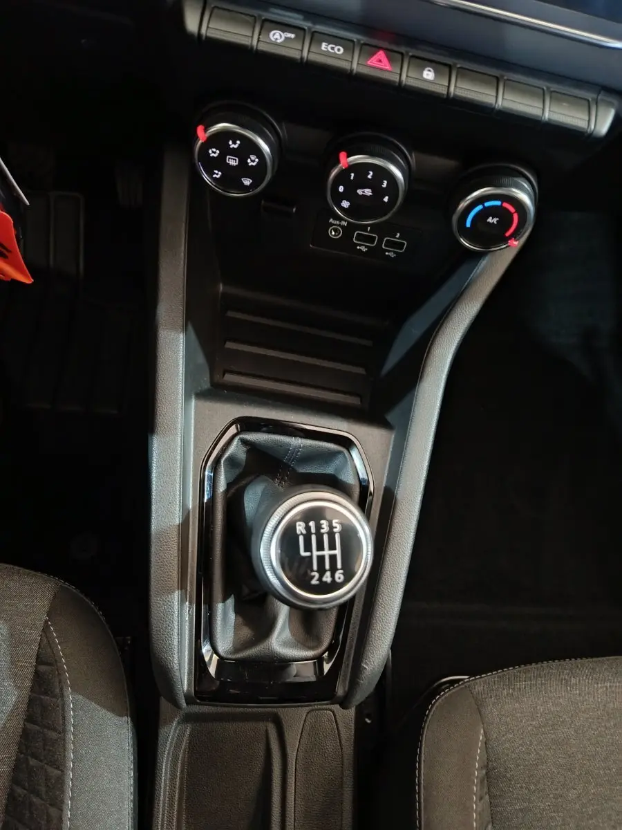 Vue plongeante sur la console centrale d’une Renault Clio gris clair 2023, avec levier de vitesse manuel et commandes de climatisation.