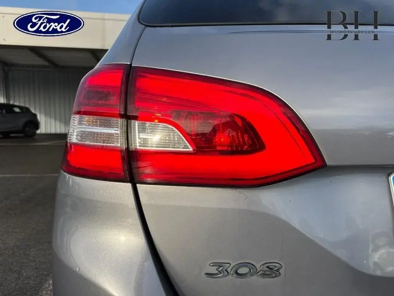 Gros plan sur le feu arrière droit rouge et blanc d'une Peugeot 308 SW gris Artense, avec logo 308 visible.