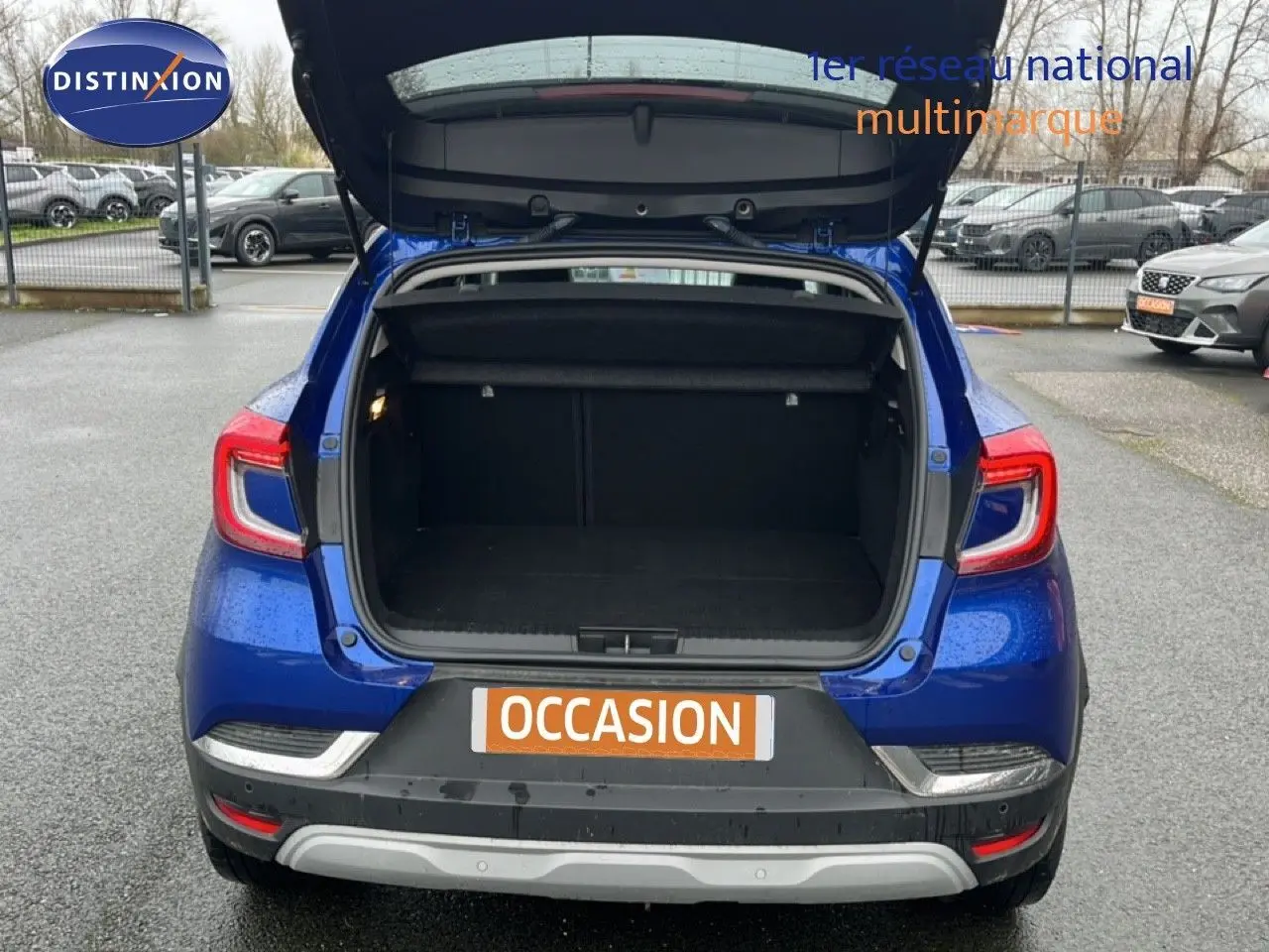 Vue arrière du Renault Captur bleu Iron Metal avec coffre ouvert, toit noir visible, sur parking extérieur.