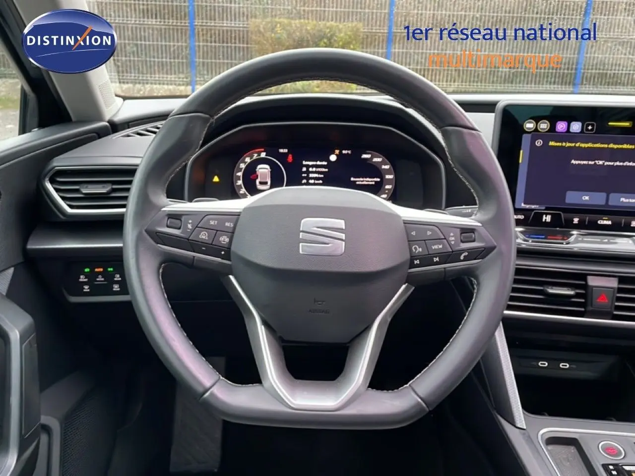 Vue intérieure centrée sur le volant cuir multifonction de la SEAT LEON ST IV 2025 avec tableau de bord numérique et écran tactile.