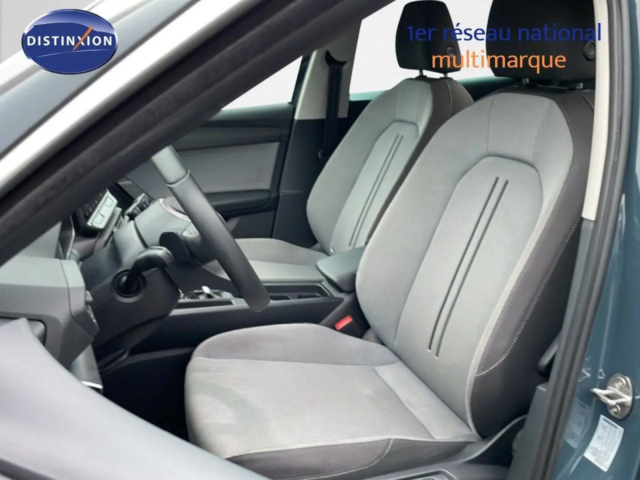 Vue intérieure côté conducteur de la SEAT LEON ST bleu fjord 2025, sièges tissu gris clair avec volant multifonction.