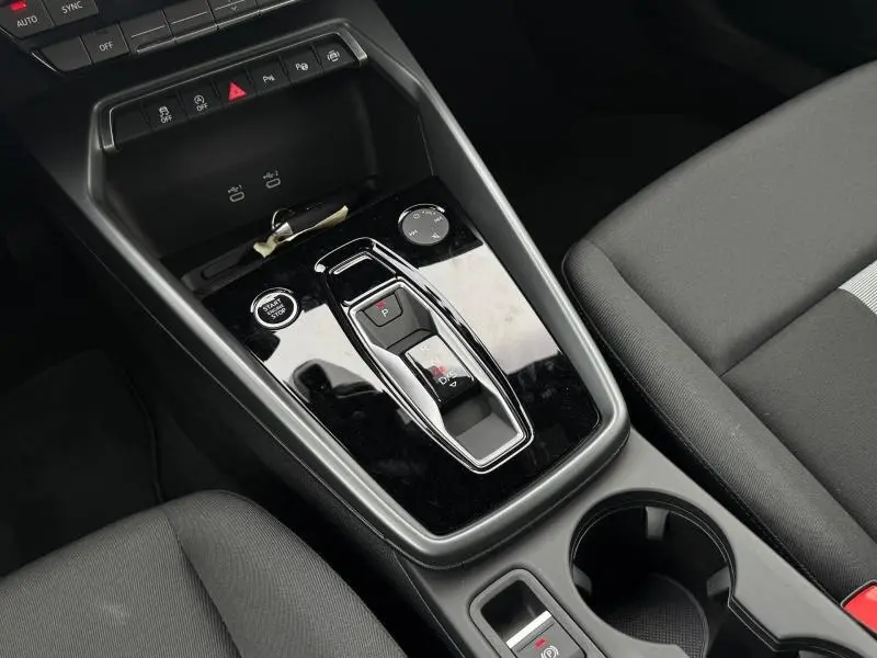 Vue plongeante sur la console centrale noire de l’Audi A3 Sportback 30 TFSI hybride avec sélecteur de boîte automatique et sièges tissu gris.