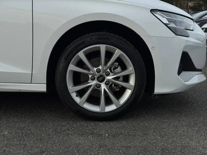 Gros plan sur la roue avant droite et partie avant blanche de l'Audi A3 Sportback 30 TFSI 2024 avec jante alu distinctive.