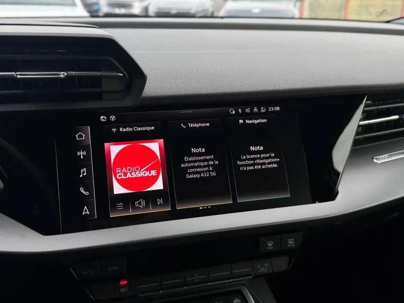 Vue rapprochée de l’écran tactile central noir de l’Audi A3 Sportback 2024 affichant la radio classique et les menus téléphone et navigation.