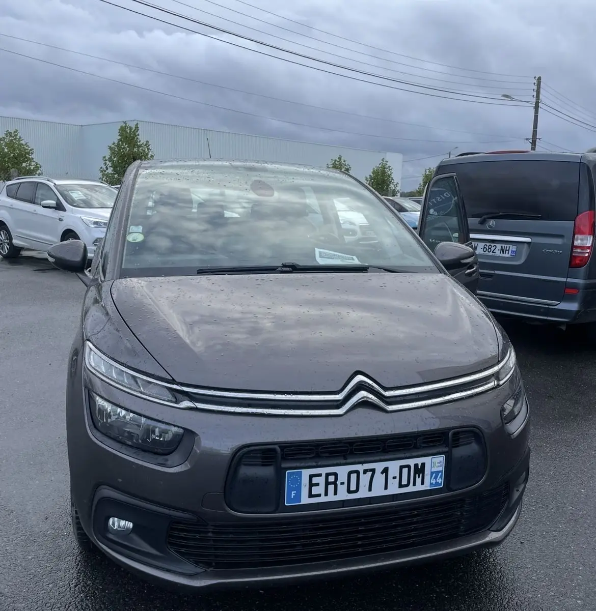 Citroën C4 Picasso marron vue de face sous la pluie, avec feux de jour LED et calandre distinctive.