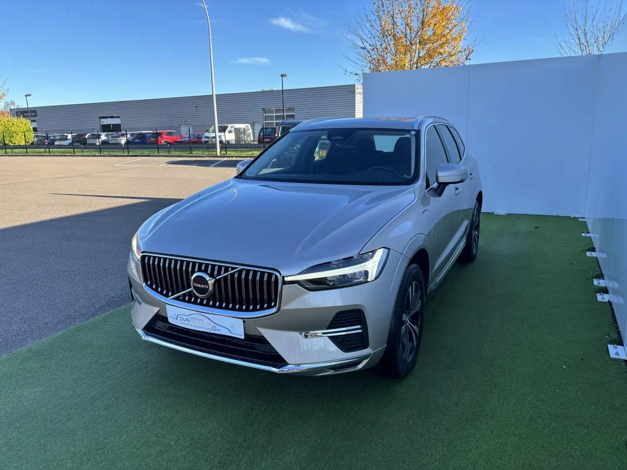 Volvo XC60 T6 Recharge argent crépuscule, vue 3/4 avant droit sur sol vert avec calandre chromée.