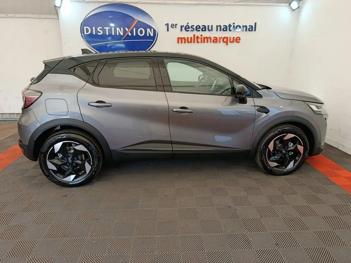 Profil droit du Renault Captur gris foncé 2025 avec jantes noires et toit noir dans un showroom intérieur.