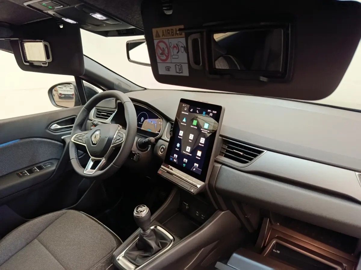 Vue intérieure côté conducteur du Renault Captur 2025, avec volant multifonctions, écran tactile vertical et levier de vitesse manuel.