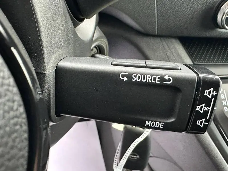 Gros plan sur la commande au volant noire du Nissan Townstar électrique 2024, avec boutons source et mode visibles.