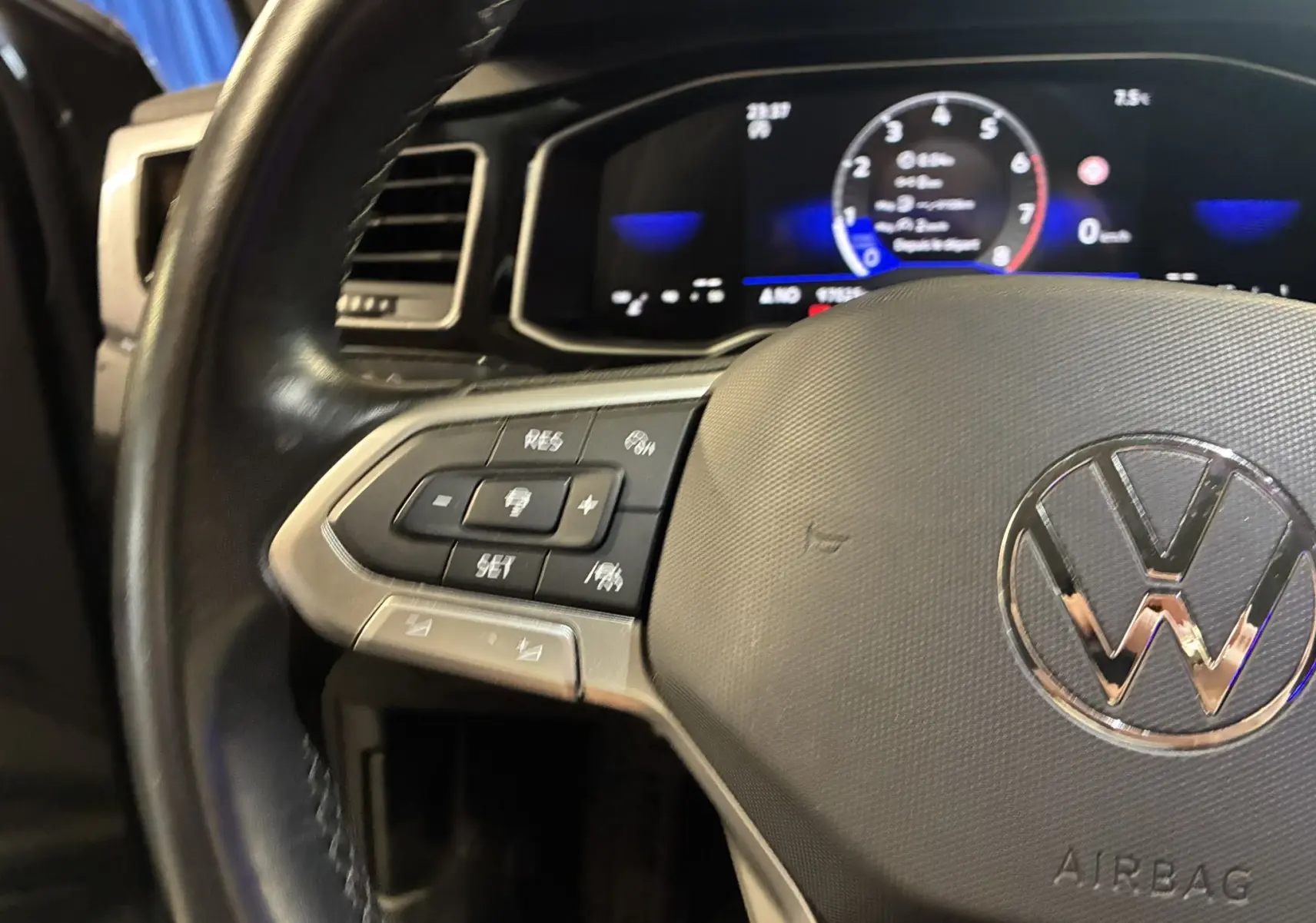 Gros plan sur le volant multifonctions gris avec logo Volkswagen et tableau de bord numérique éclairé en arrière-plan.