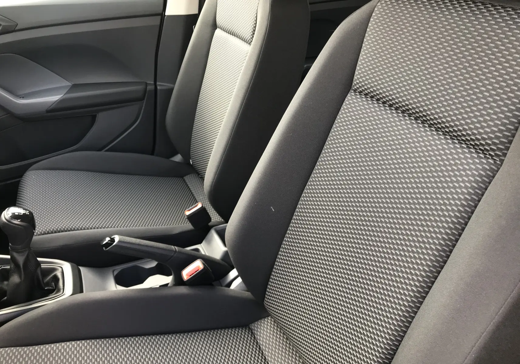 Gros plan sur les sièges avant en tissu noir et gris du Volkswagen T-Cross 2020 avec levier de vitesse manuel visible.