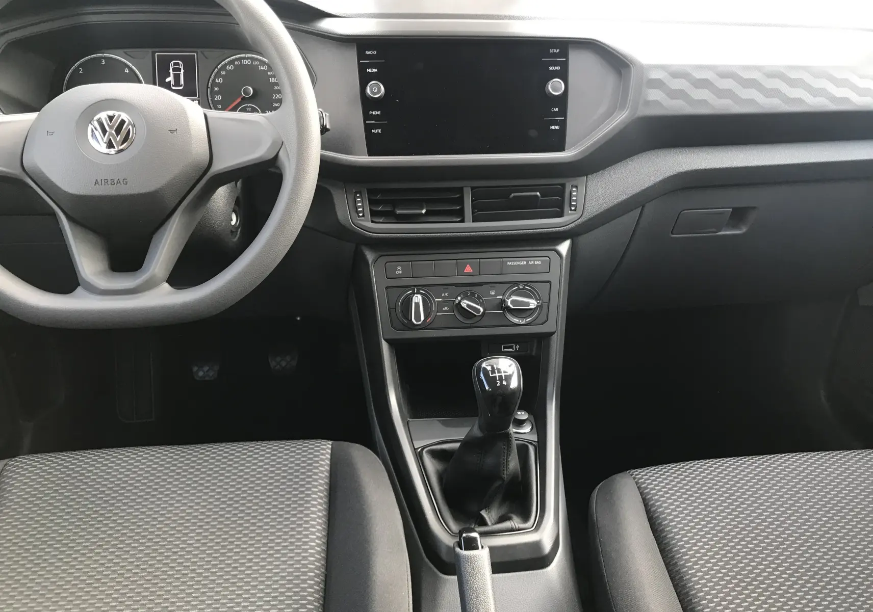Vue intérieure frontale du Volkswagen T-Cross 2020 gris Limestone, montrant le volant, la console centrale avec boîte manuelle et écran tactile.