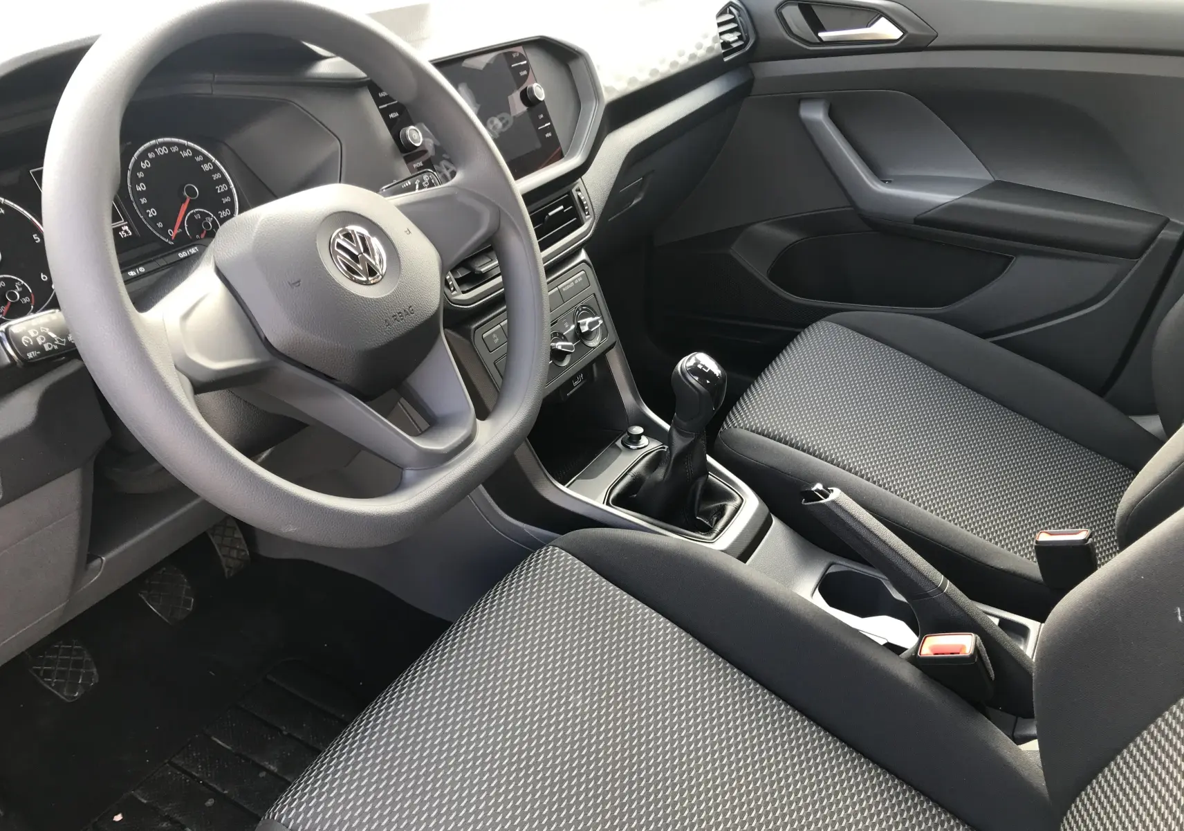 Intérieur avant droit du Volkswagen T-Cross 2020 avec volant, tableau de bord gris et sièges tissu noir à motifs.