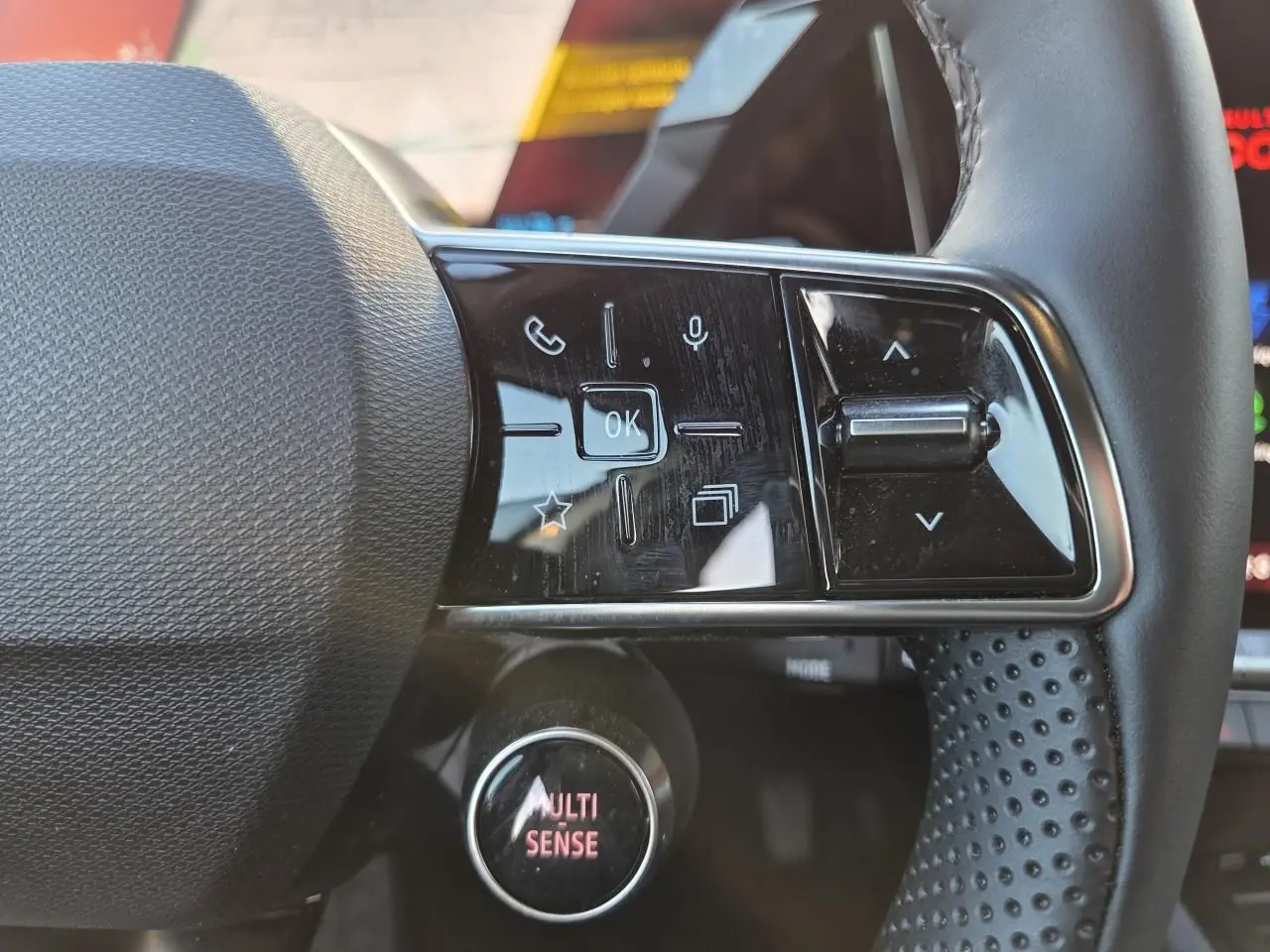Gros plan sur les commandes du volant textile grainé du Renault Austral 2025, avec bouton MULTI-SENSE éclairé.