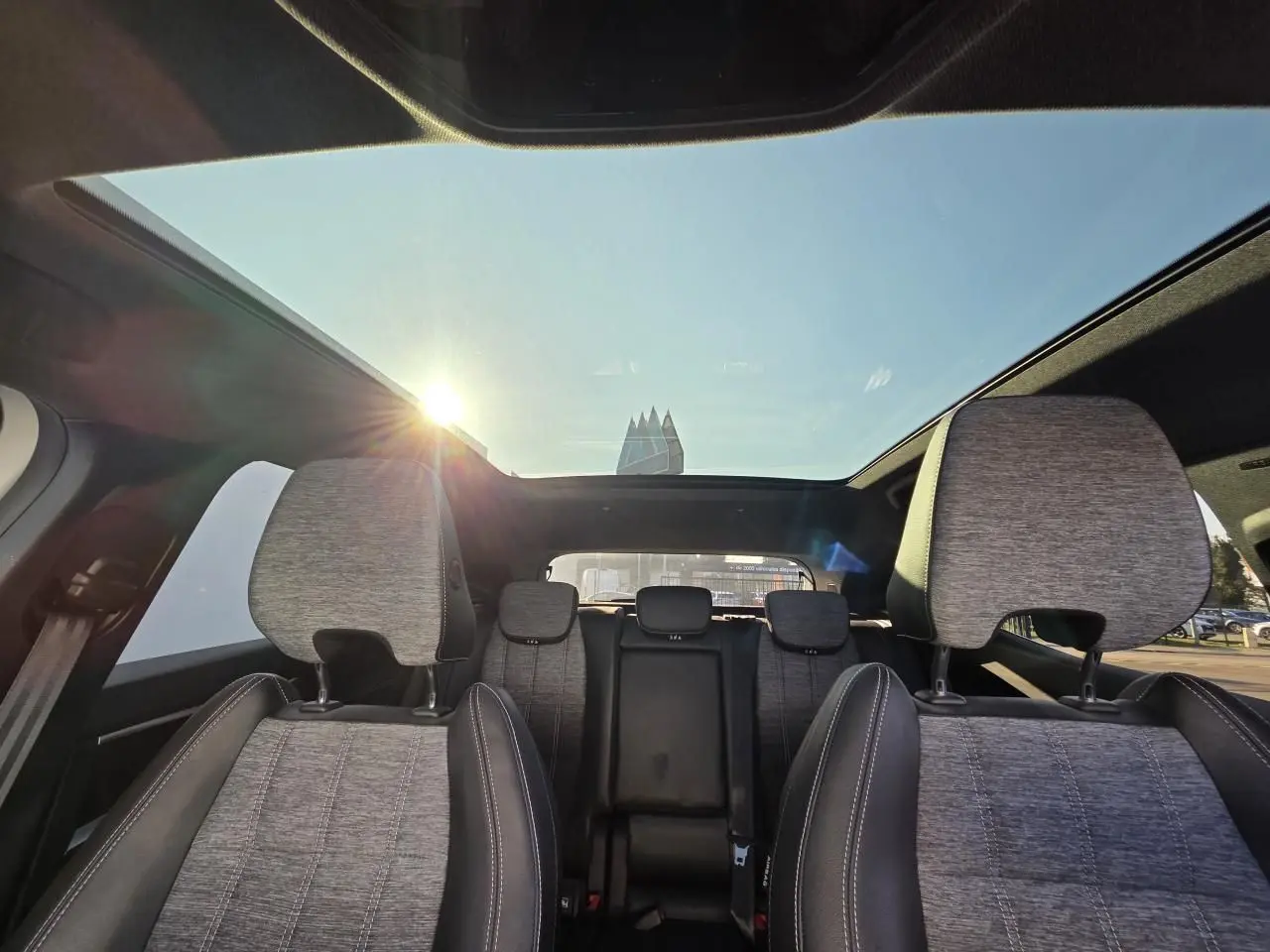 Vue intérieure arrière du Renault Austral 2025 avec sièges gris et toit panoramique en verre laissant passer la lumière du soleil.