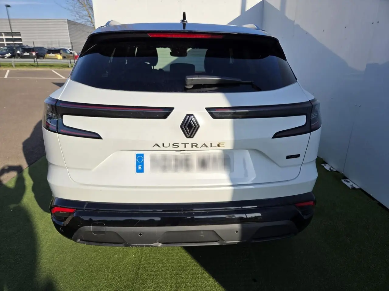 Vue arrière d'un Renault Austral blanc nacré avec toit noir, feux arrière LED et logo centré sur un parking.