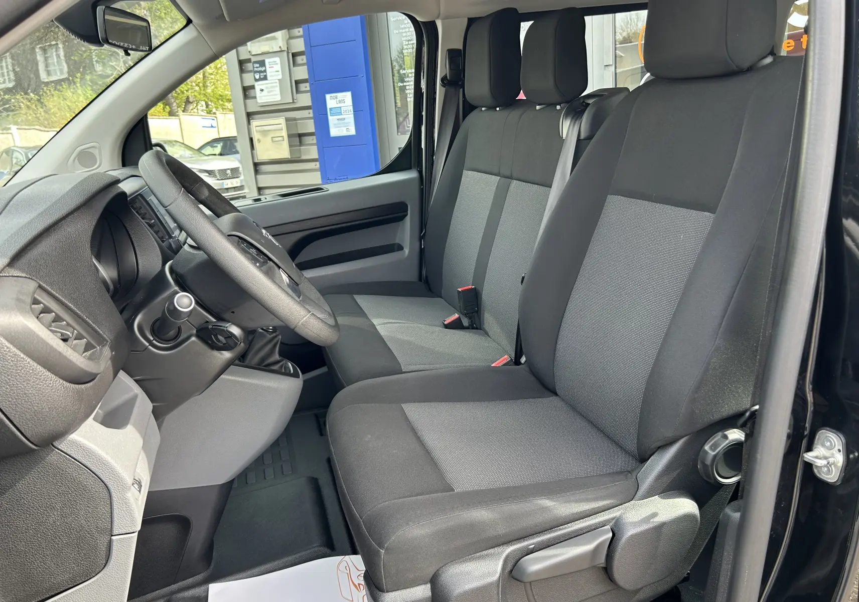 Vue intérieure côté conducteur de l’Opel Vivaro Combi noir 2022, montrant les sièges tissu bicolore et le volant.