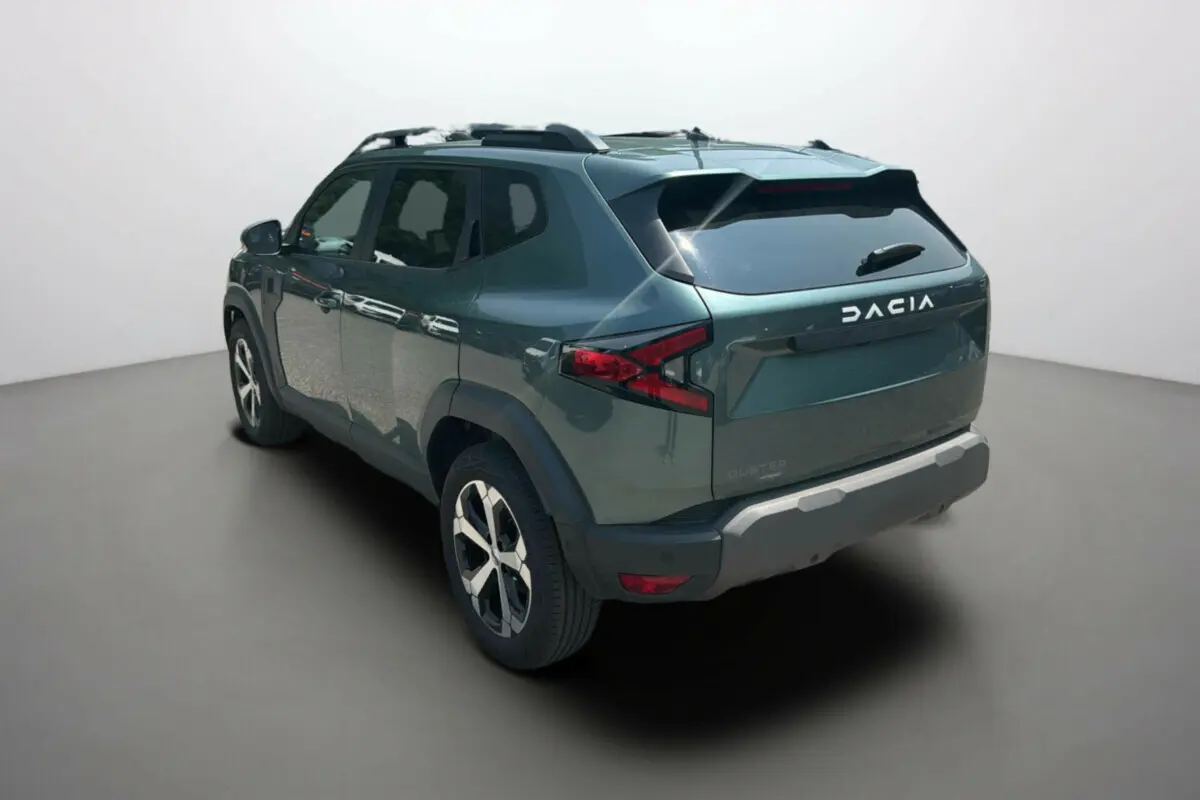 Vue 3/4 arrière droite du Dacia Duster 2025 vert cèdre avec jantes alu 18 pouces et barres de toit visibles.