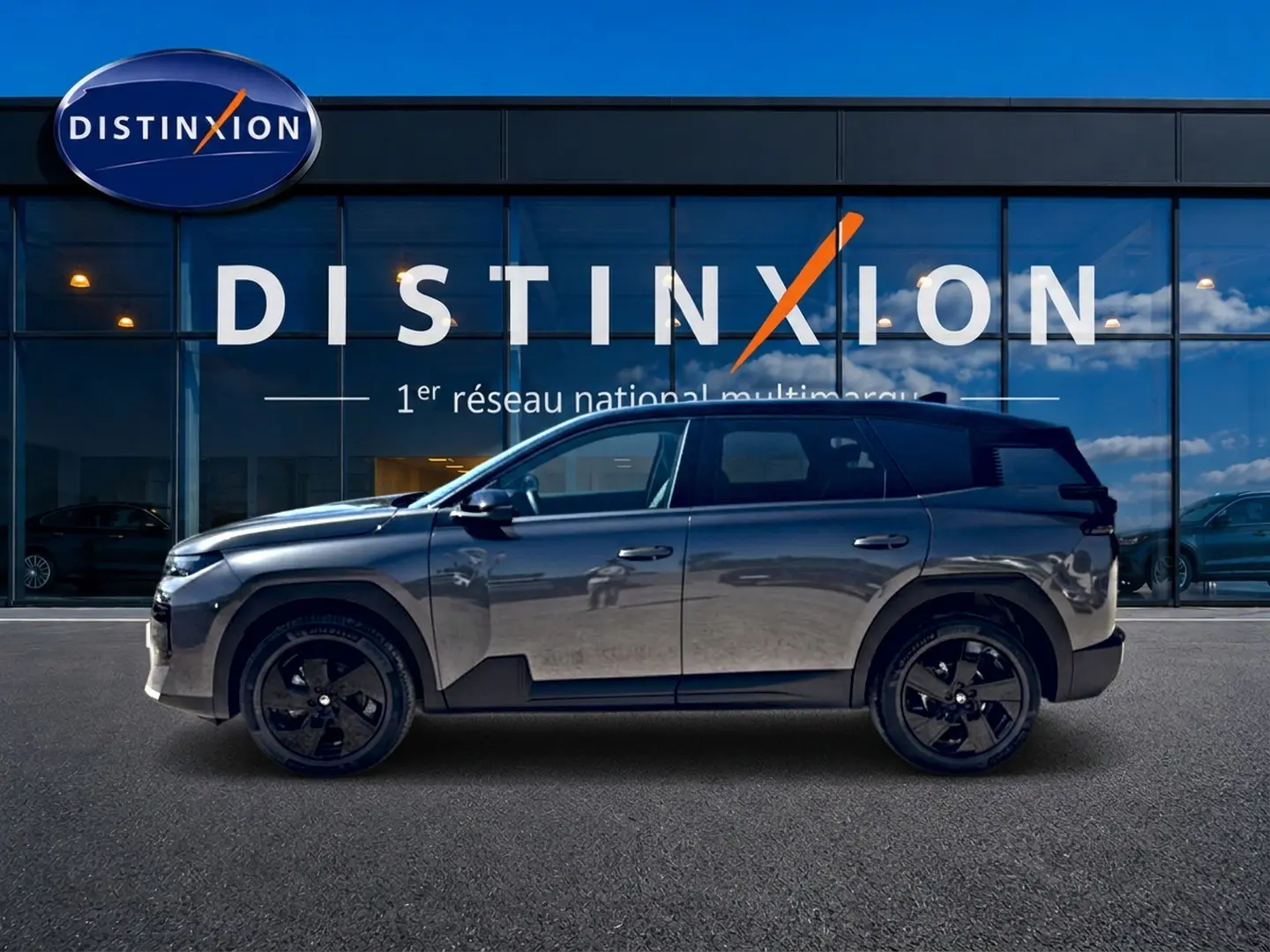 Profil droit du Citroën C5 Aircross gris platinium avec toit noir et jantes alliage noires devant une vitrine Distinxion.