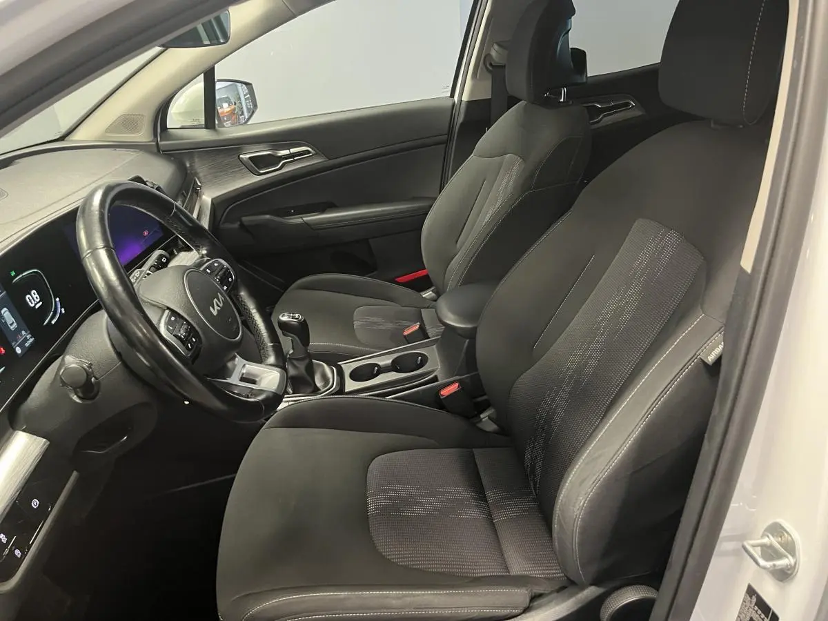 Vue intérieure côté conducteur du Kia Sportage blanc 2022, sièges noirs avec volant cuir et tableau de bord digital.