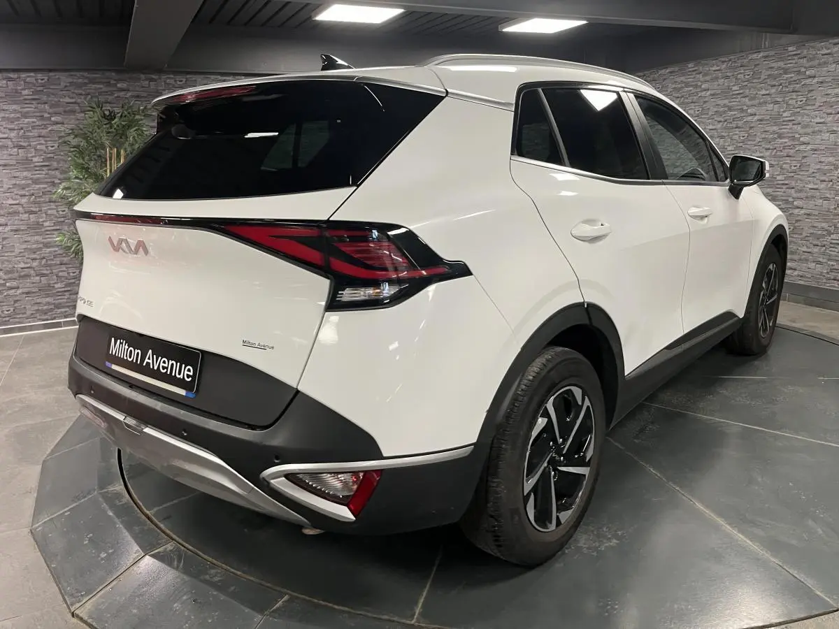Vue 3/4 arrière droite d'un KIA Sportage blanc nacré avec jantes alliage noires et vitres surteintées.