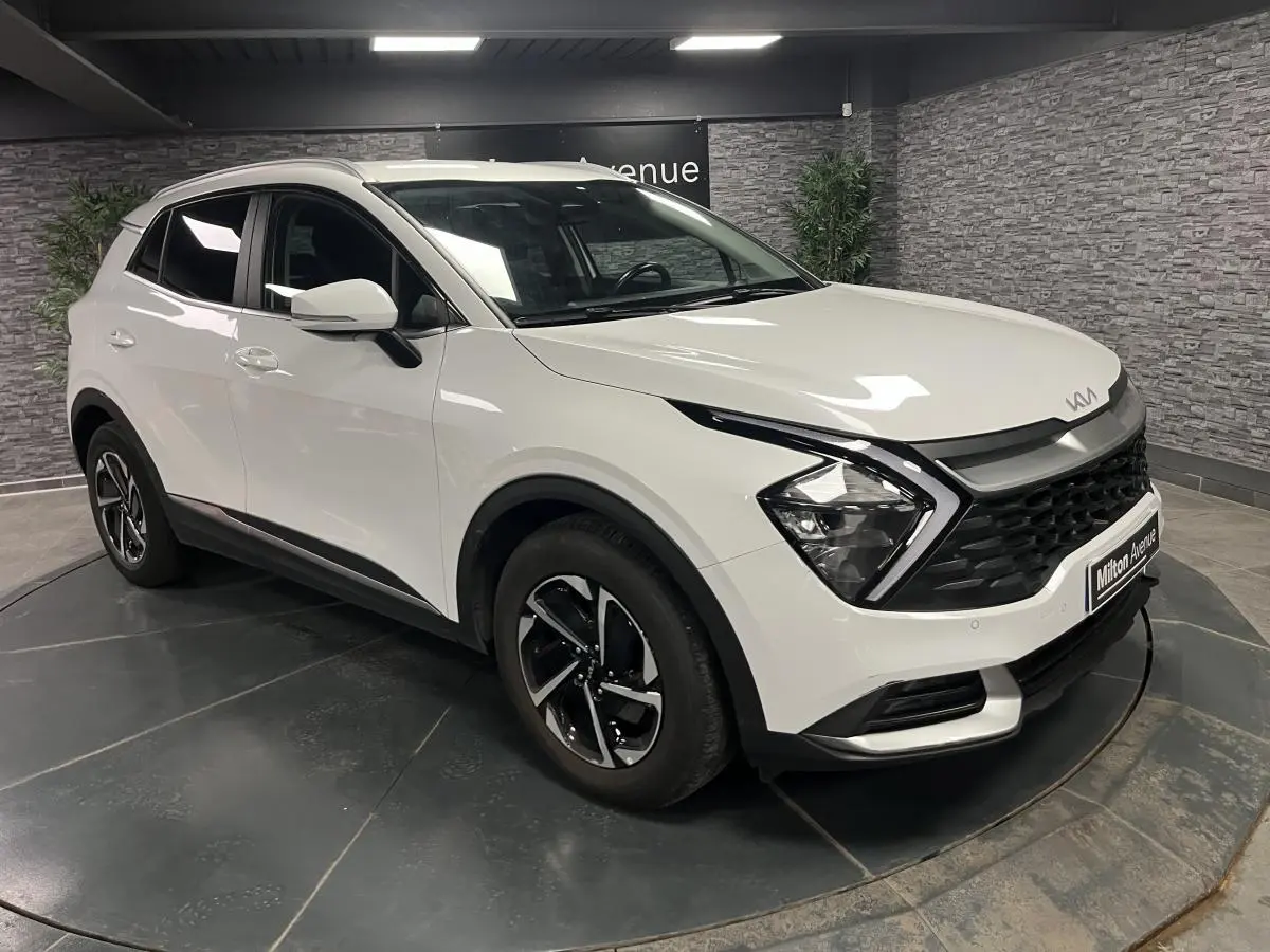 KIA Sportage blanc nacré en 3/4 avant droit, avec calandre noire laquée et jantes alliage 18 pouces.