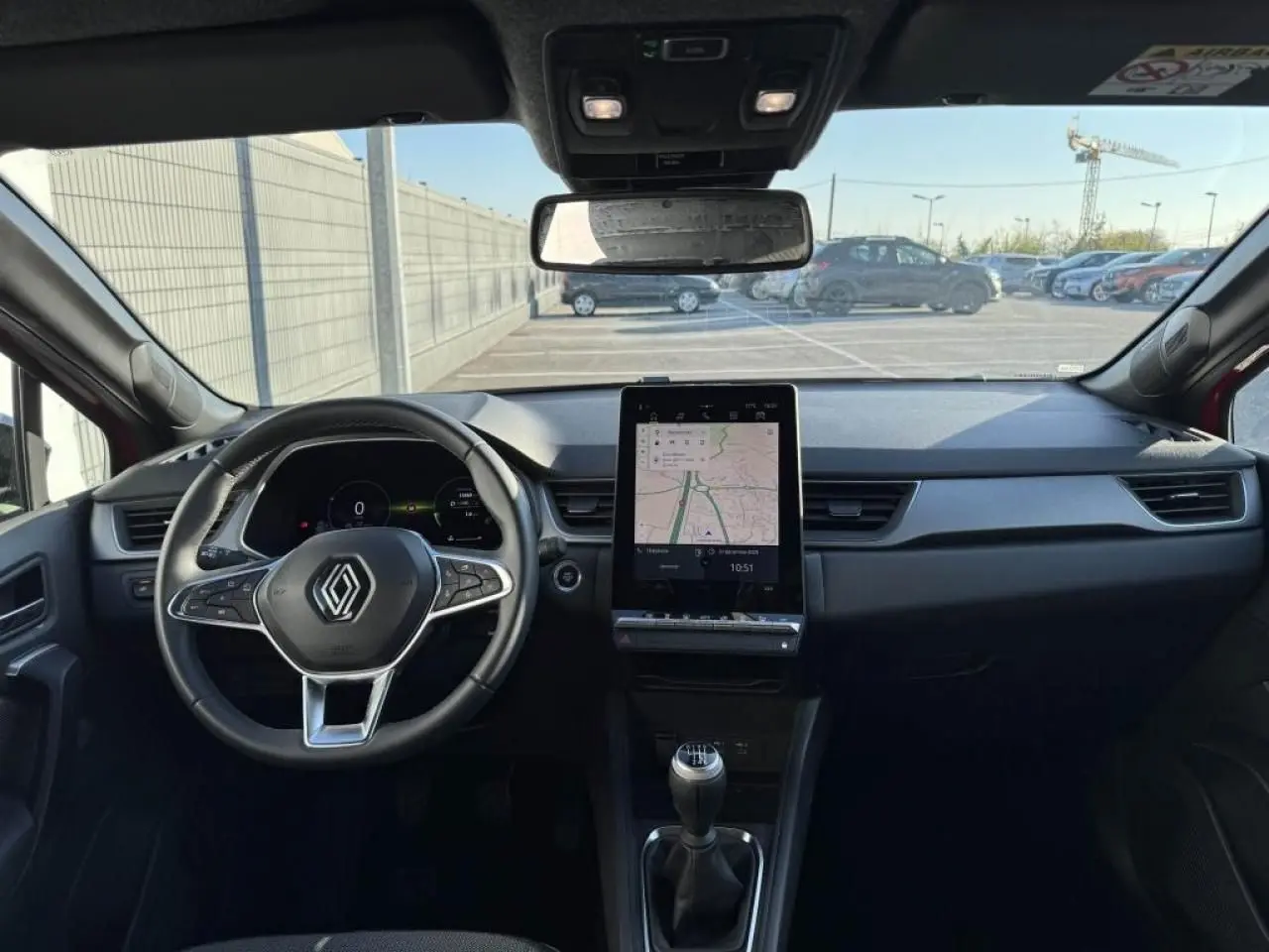 Vue intérieure avant du Renault Captur II rouge flamme, montrant le volant, écran tactile vertical et levier de vitesse manuel.