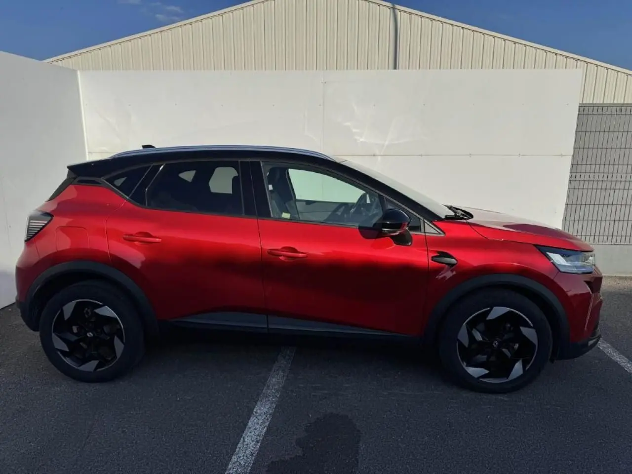 Vue de profil côté gauche du Renault Captur II rouge flamme avec toit noir et jantes noires en aluminium.