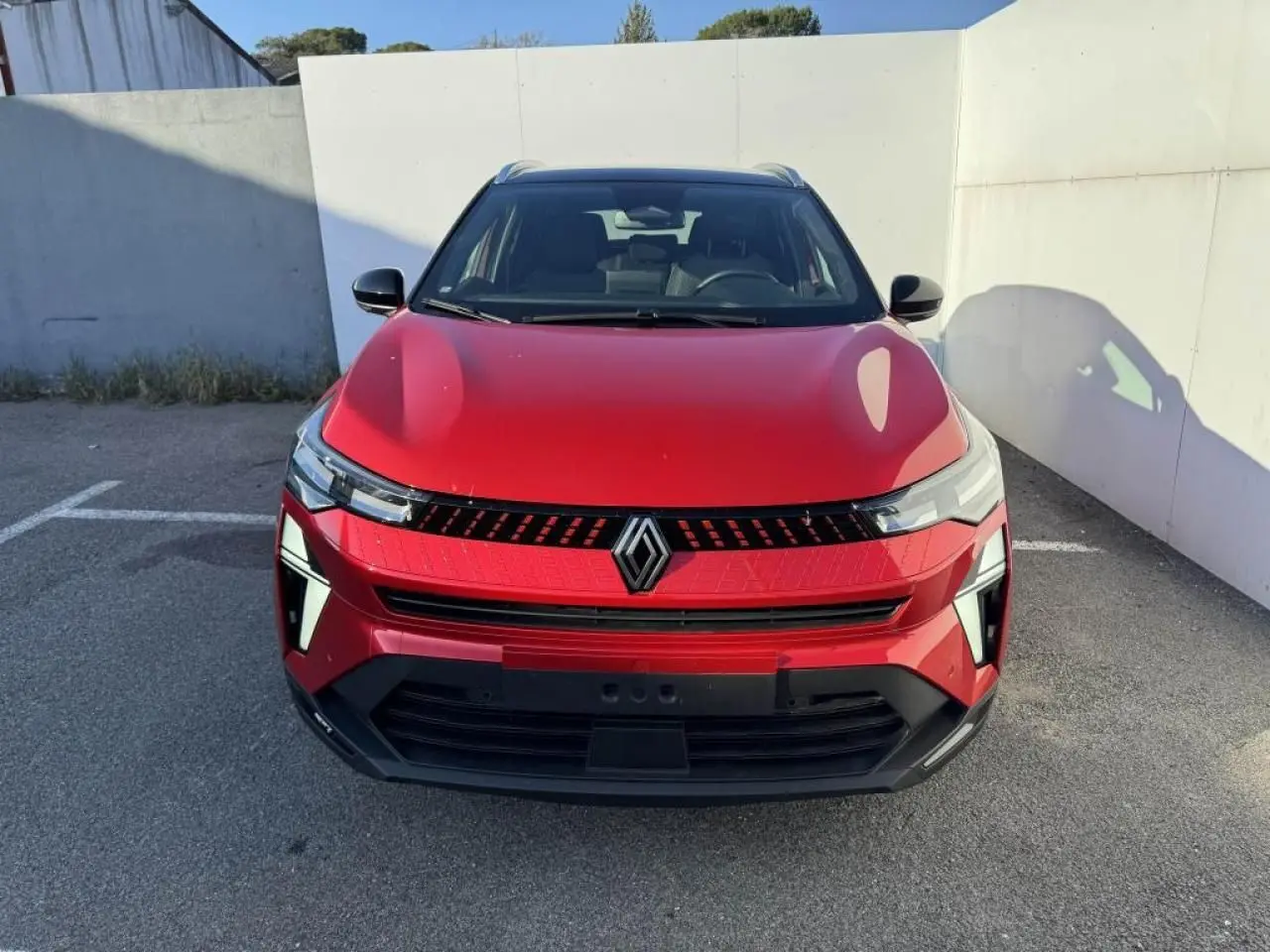 Vue avant d'un Renault Captur II rouge flamme avec toit noir, mettant en valeur sa calandre moderne et ses phares LED.