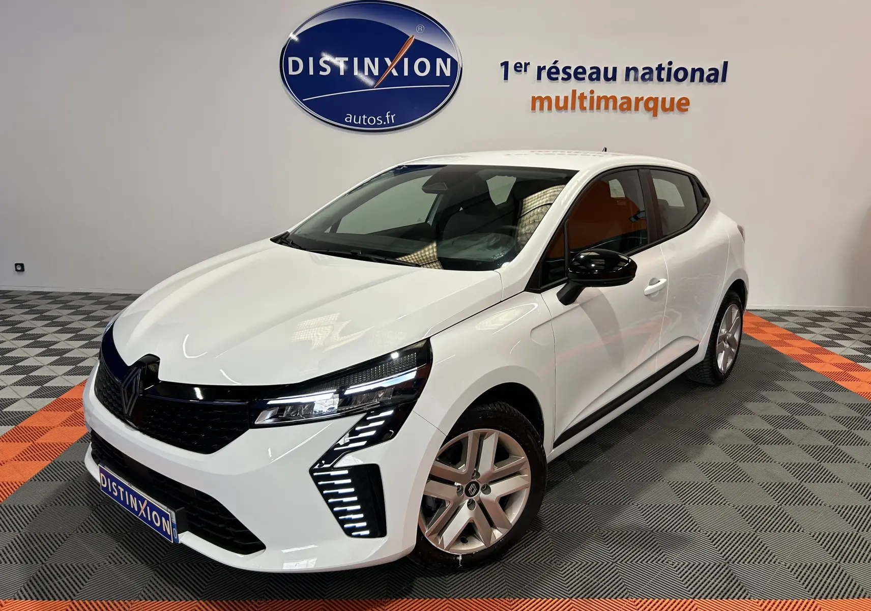 Renault Clio V blanc vue 3/4 avant droit en showroom avec feux LED et rétroviseurs noirs.